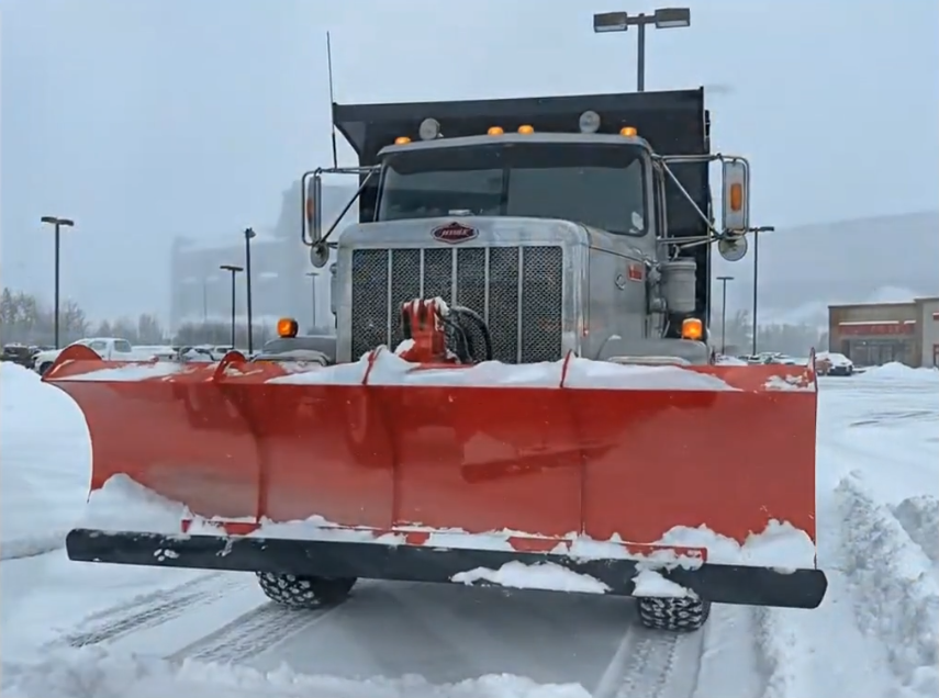 Red snow plow on a Tuscano truck in a commercial parking lot